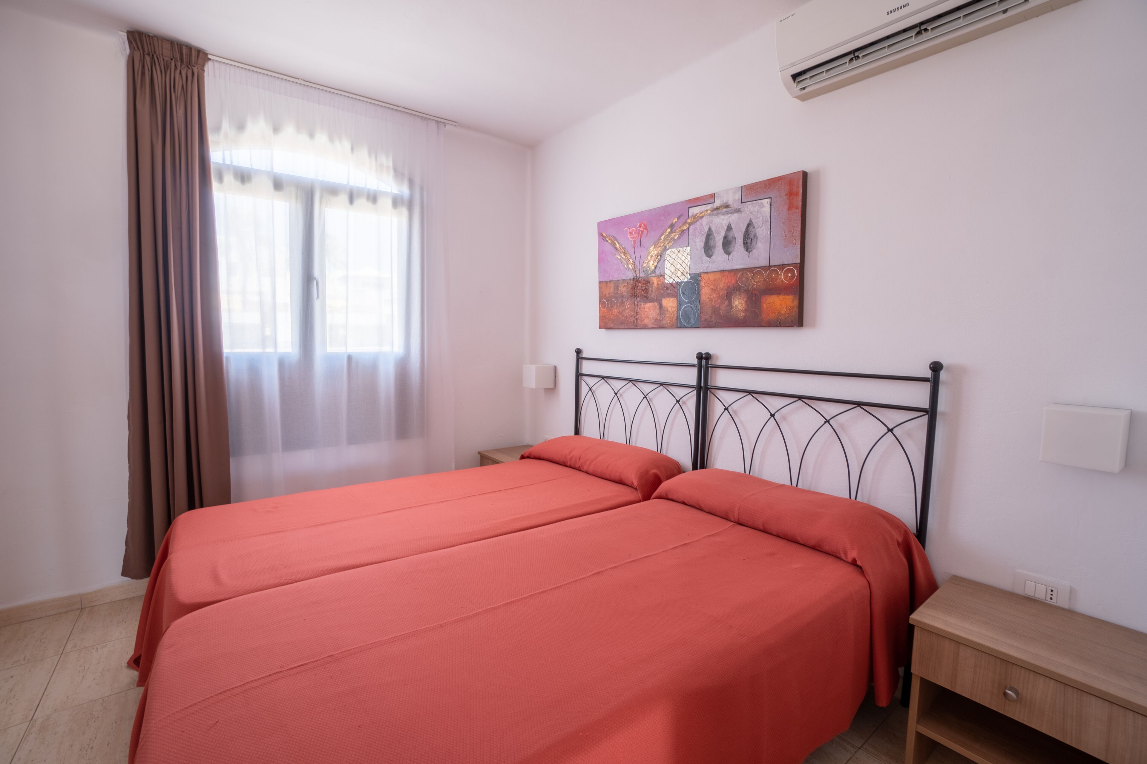 Een slaapkamer met een bed, nachtkastje, wandairconditioner en een raam met gordijnen.