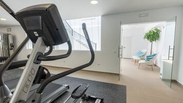 Un gimnasio con una cinta de correr, una escaladora y una puerta de cristal que da a una zona de estar con sillas y una planta.