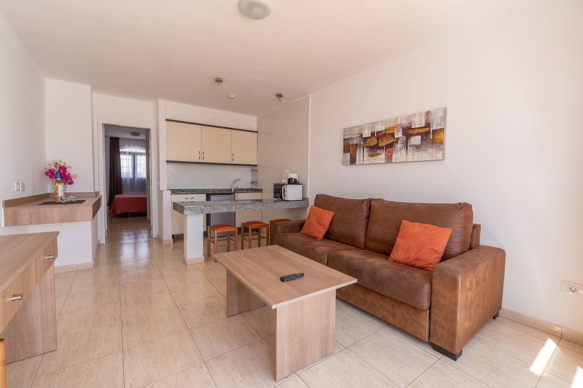 Ein modernes Wohnzimmer mit einer braunen Ledersofa, einem Holztisch und einer Küchenzeile im Hintergrund.