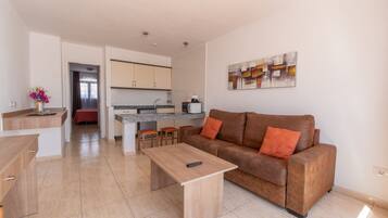 Una sala de estar moderna con un sofá de cuero marrón, una mesa de centro de madera y una cocina al fondo.