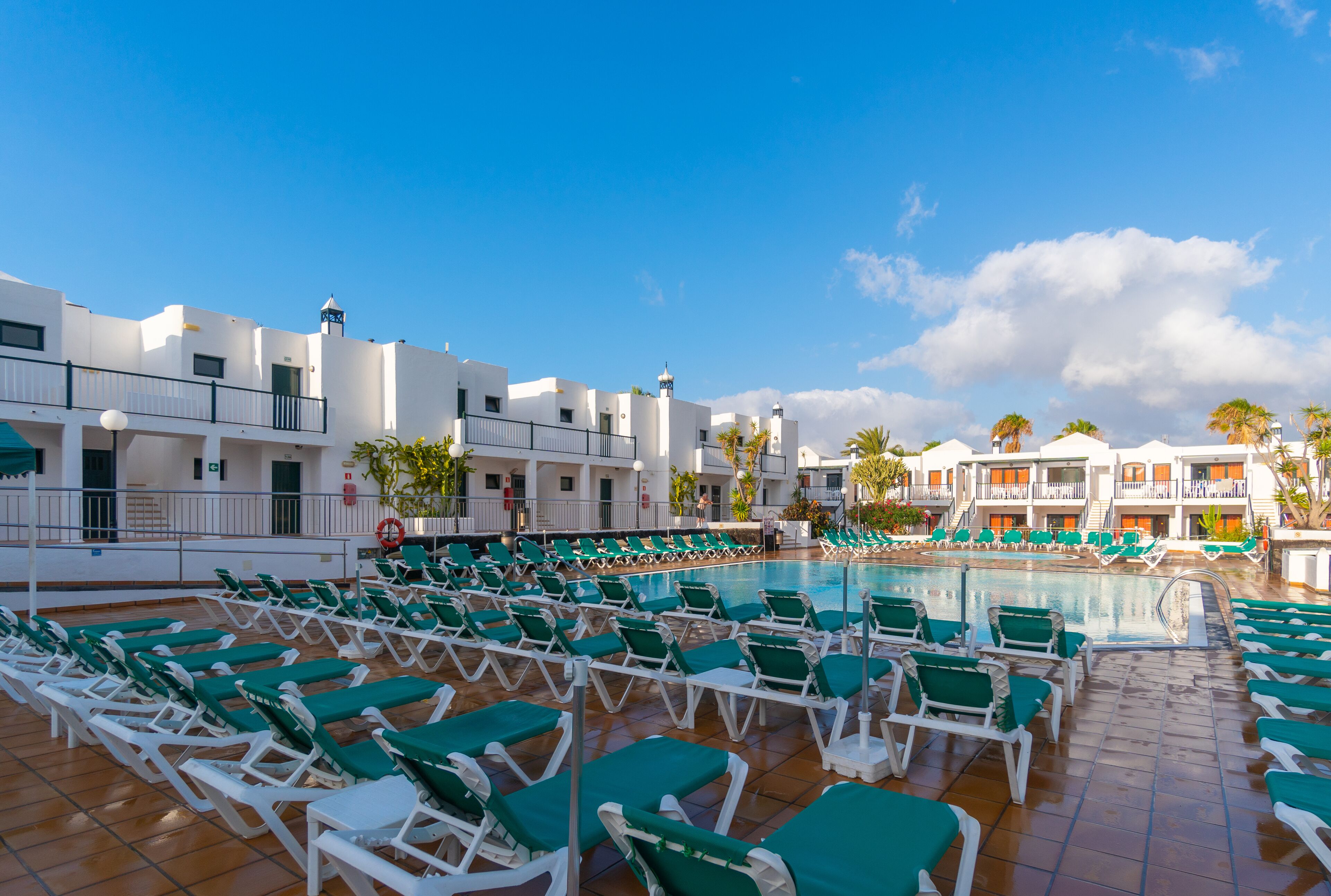 Zona de piscina con filas de sillones de sol y un cielo azul despejado.