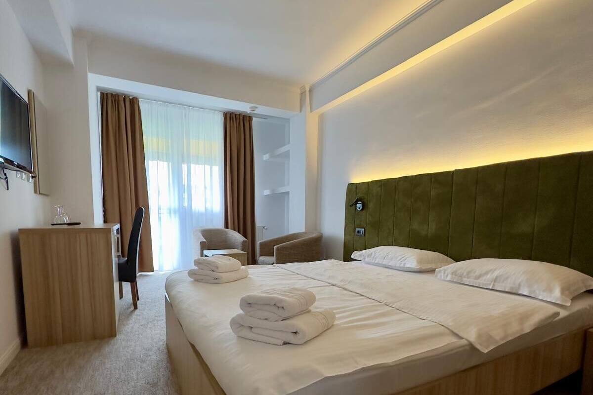 A hotel room with a large bed, a TV, a desk, and a window with curtains.