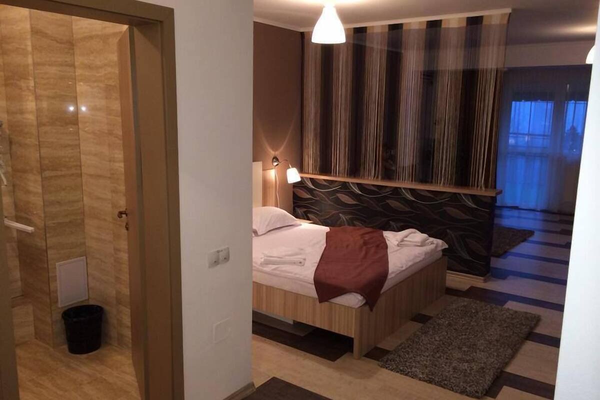 A modern hotel room with a wooden bed, a small rug, and a striped curtain.