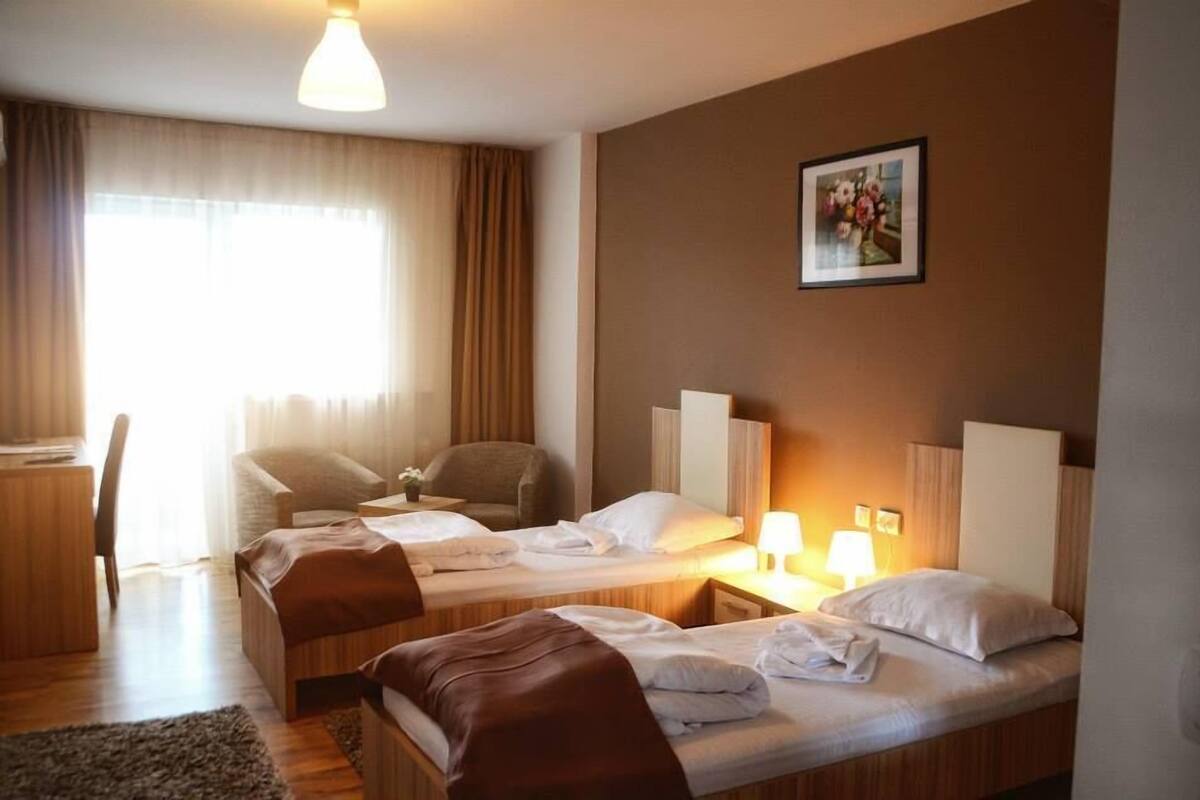 A hotel room with two beds, a desk, a chair, and a window with curtains.