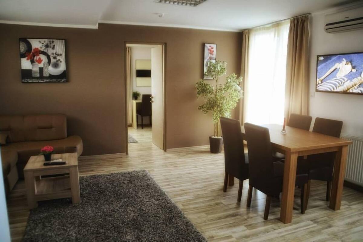 A living room with a sofa, a coffee table, a dining table with chairs, a potted plant, and artwork on the walls.
