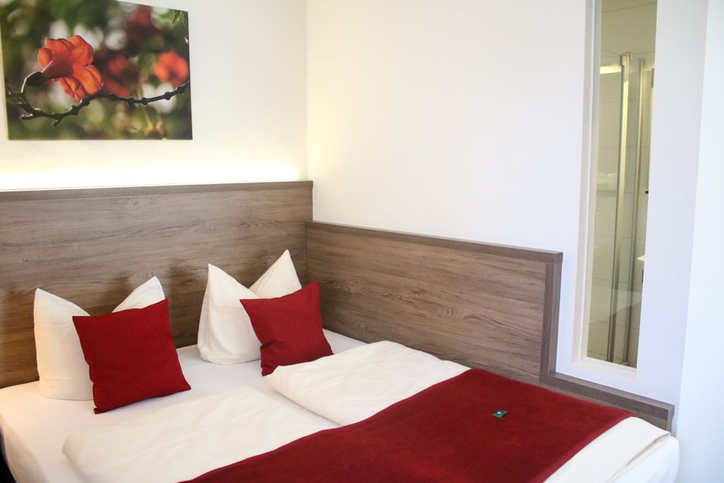 A hotel room with a wooden headboard, a bed with white and red bedding, and a framed picture of flowers on the wall.