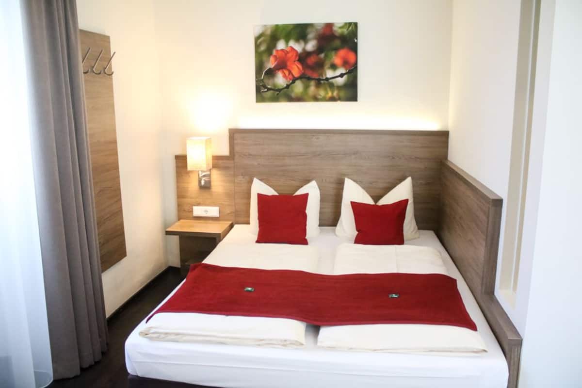 Un lit double avec des oreillers rouges, une tête de lit en bois, une table de chevet avec une lampe et un tableau de fleurs accroché au mur.