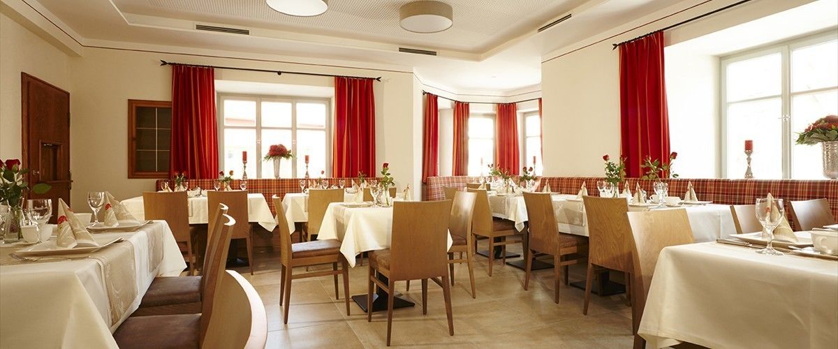 Un restaurante con varias mesas dispuestas para comer, con cortinas rojas y manteles blancos.