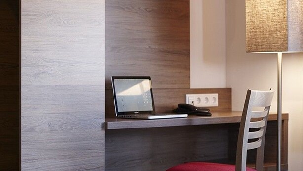 A hotel room with a bed, a desk with a laptop, a chair, and a lamp.