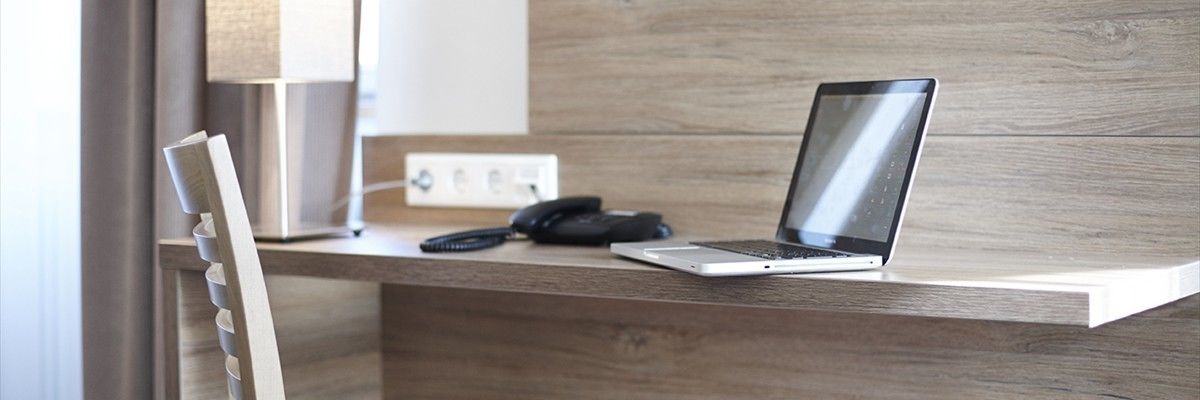 A laptop on a wooden desk with a telephone and a power outlet.