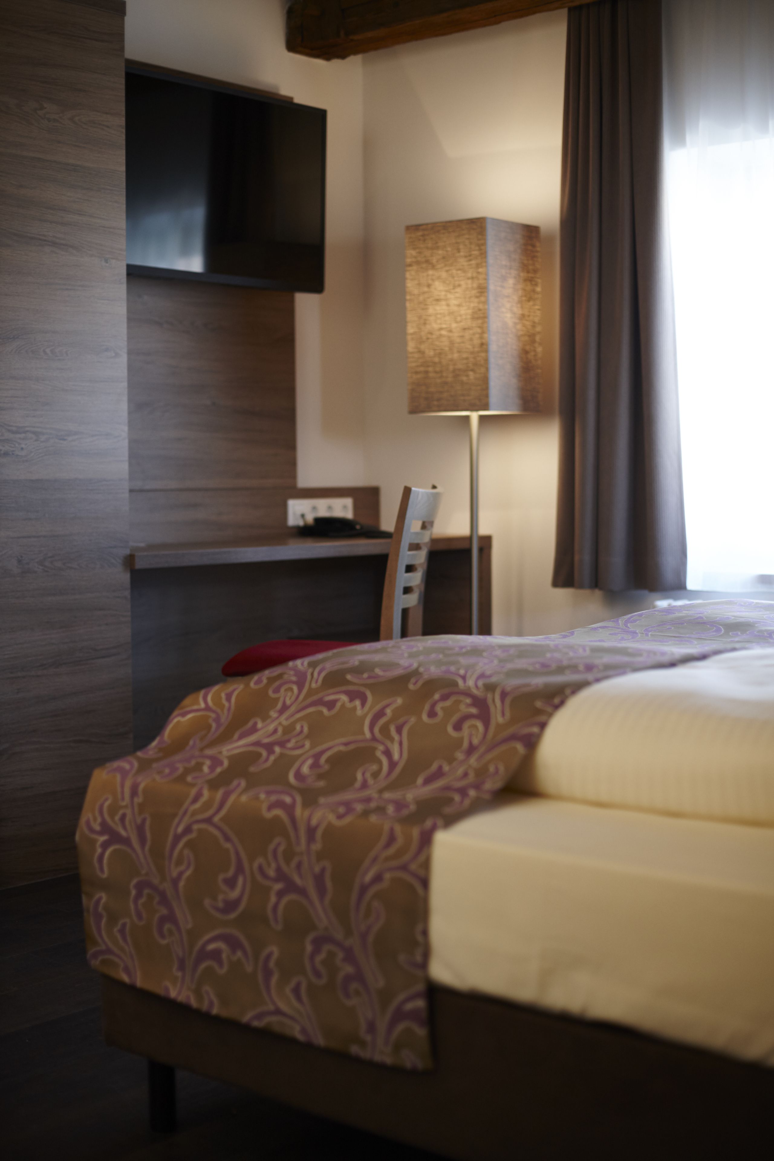 Une chambre d’hôtel comprenant un lit, un bureau, une chaise, une lampe et un téléviseur.