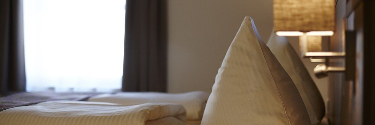 Et hotelværelse med en pænt redt seng, en lampe på sengebordet og et vindue med gardiner.