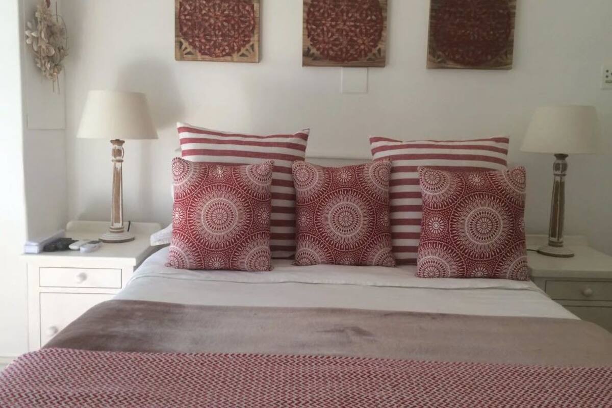 A neatly made bed with patterned pillows and a white headboard. There are three wall-mounted artworks above the bed.