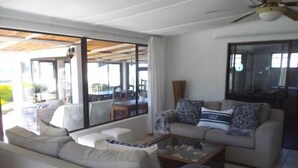 Amplia sala de estar con un sofá, sillones y una mesa de centro. Amplias ventanas ofrecen vistas al exterior.