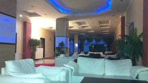 Un hall con sofás de cuero blanco, un mostrador de recepción y una pantalla grande.