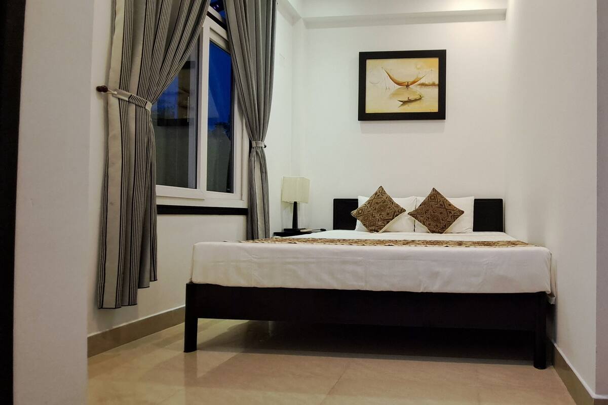 A bedroom with a bed, a bedside table, a lamp, and a framed picture on the wall.