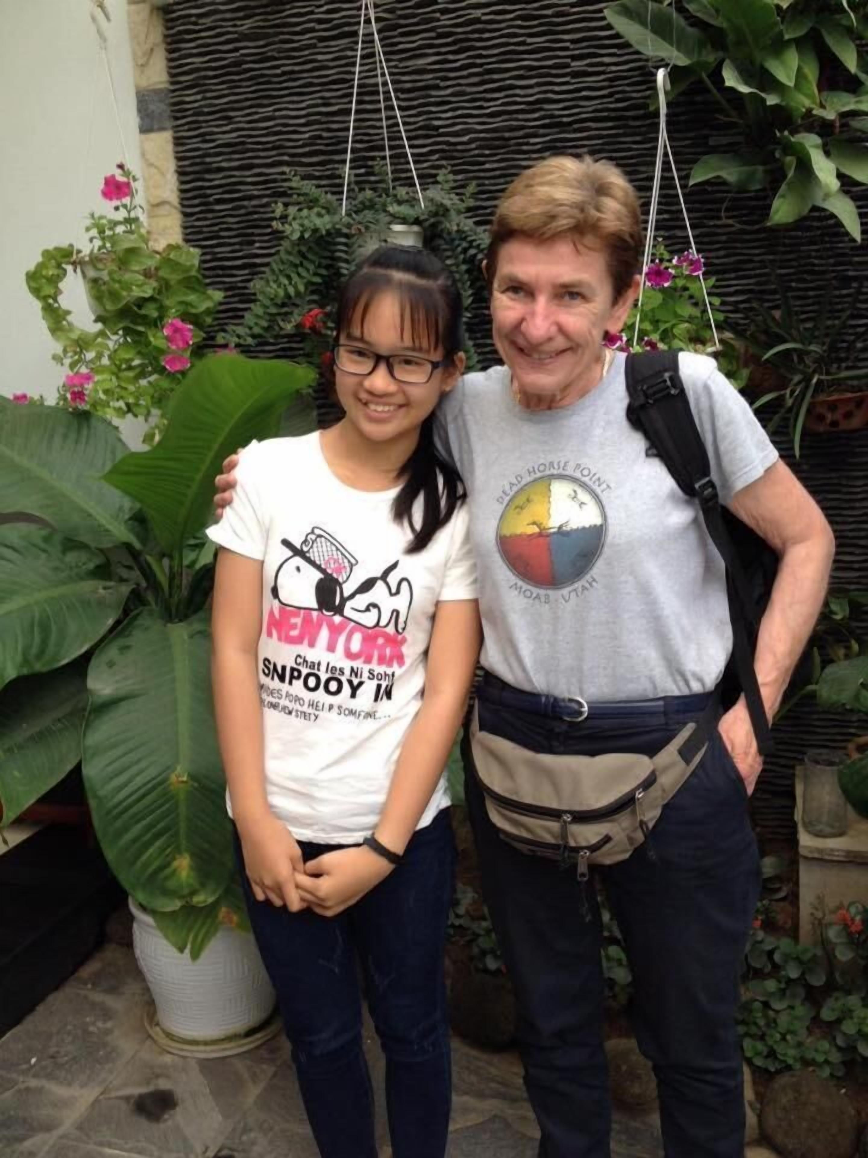 Zwei Personen stehen in einem Garten mit Topfpflanzen und einer Steinmauer im Hintergrund.