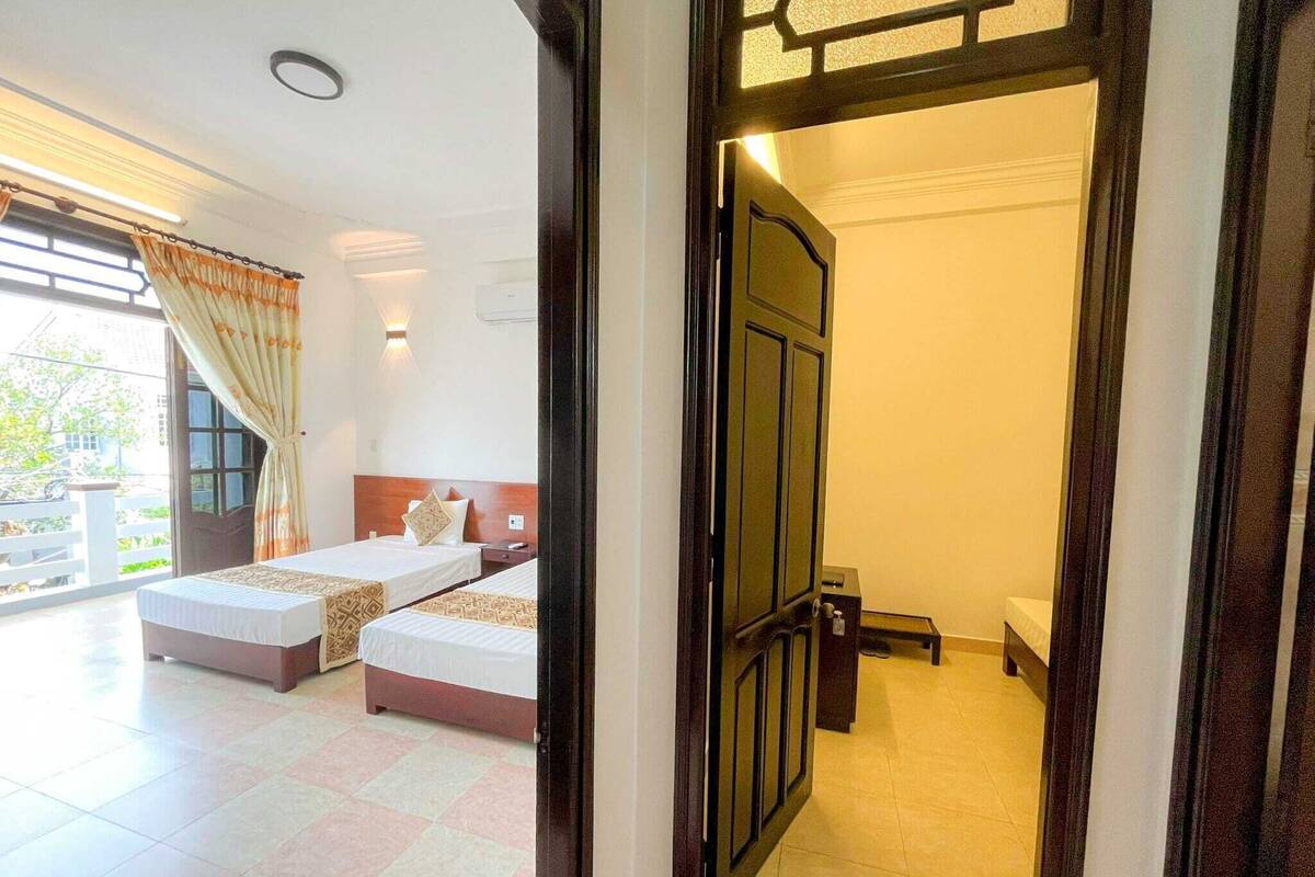 A hotel room with two beds, a balcony, and a view of the outdoors.