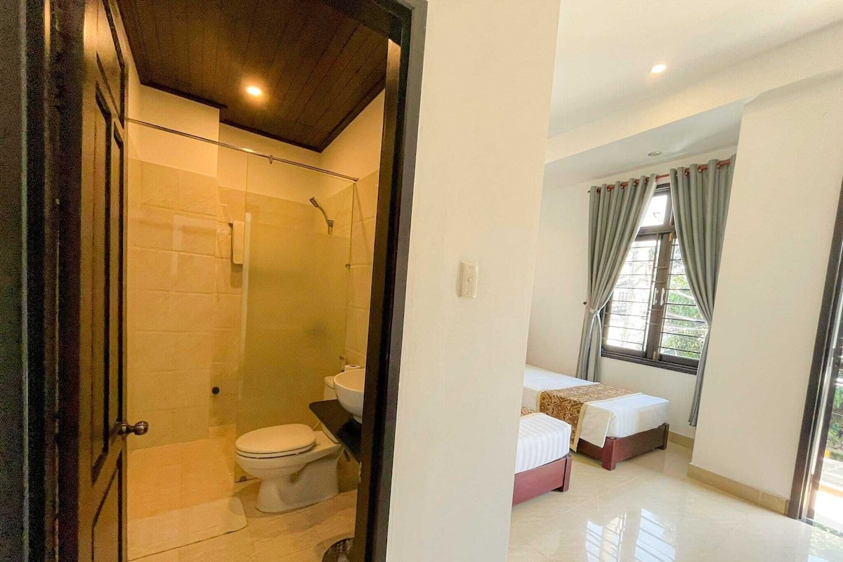 A hotel room with a shower, toilet, and two beds.
