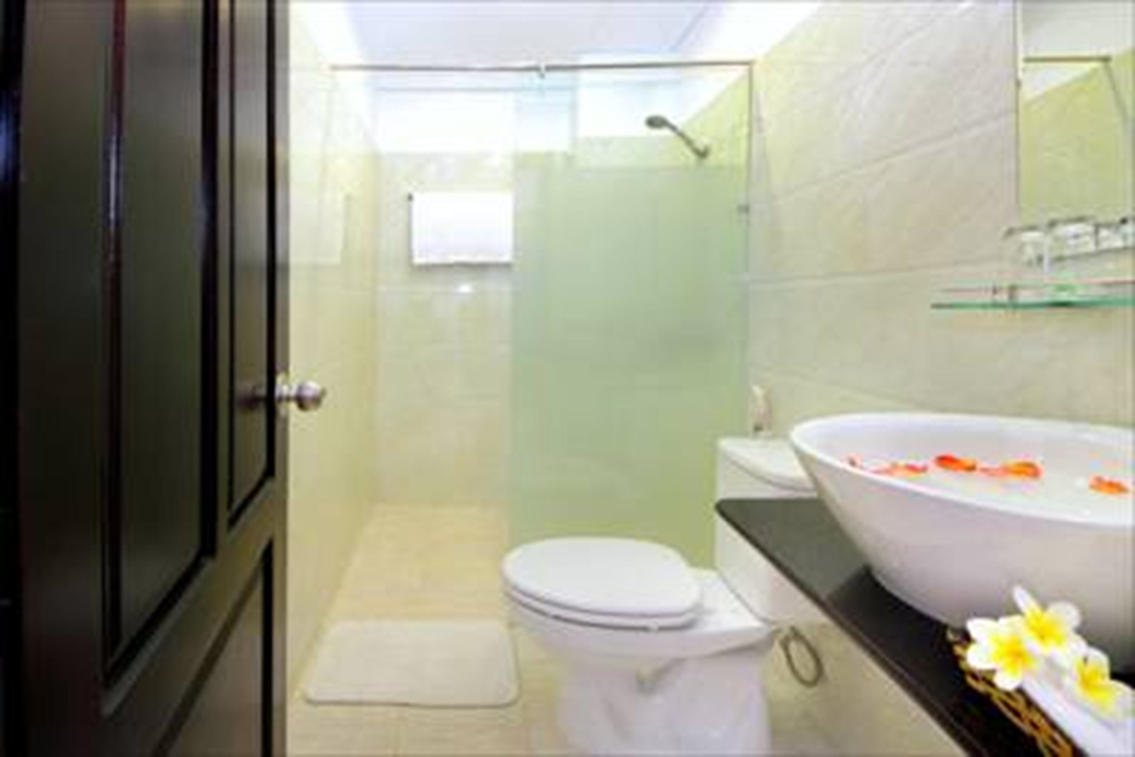 A bathroom with a glass shower enclosure, a white toilet, and a large oval sink with flower petals.