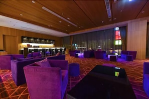 Eine moderne Hotelhalle mit violetten Sitzgelegenheiten, einer Bar und großen Fenstern mit Blick auf die Stadt.