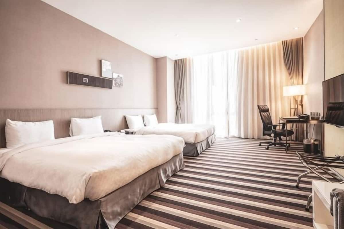 Una habitación de hotel con dos camas, televisión, escritorio y un ventanal grande con cortinas.