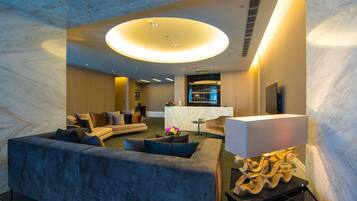 A modern hotel lobby with a curved sofa, a round coffee table, and a bar area.