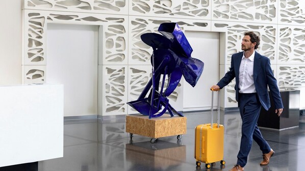 A modern interior with a geometric wall design, a wooden sculpture, and a person pulling a suitcase.