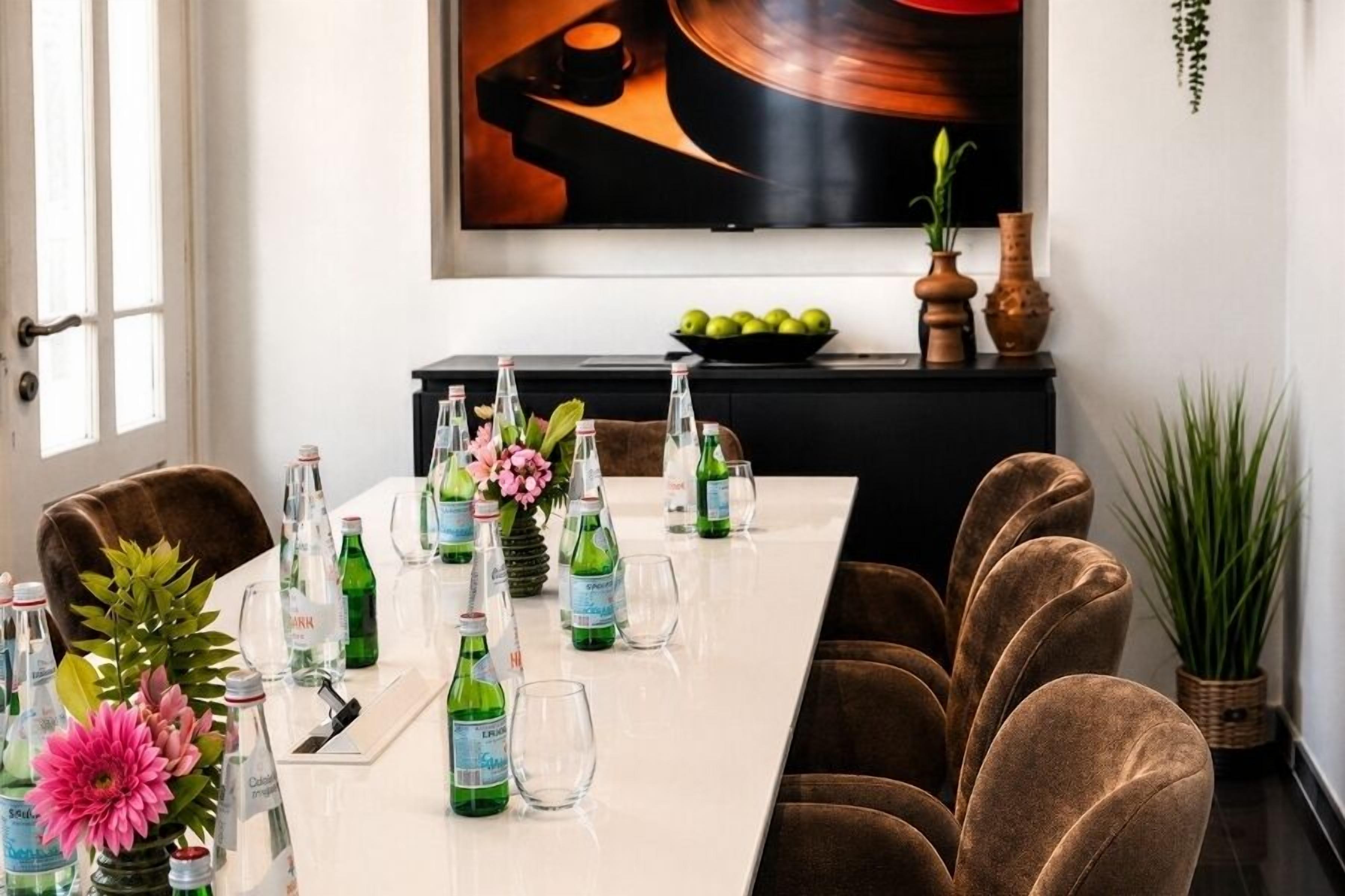 A dining table set with bottles and glasses, a vase with flowers, and a bowl of fruit on a black cabinet.