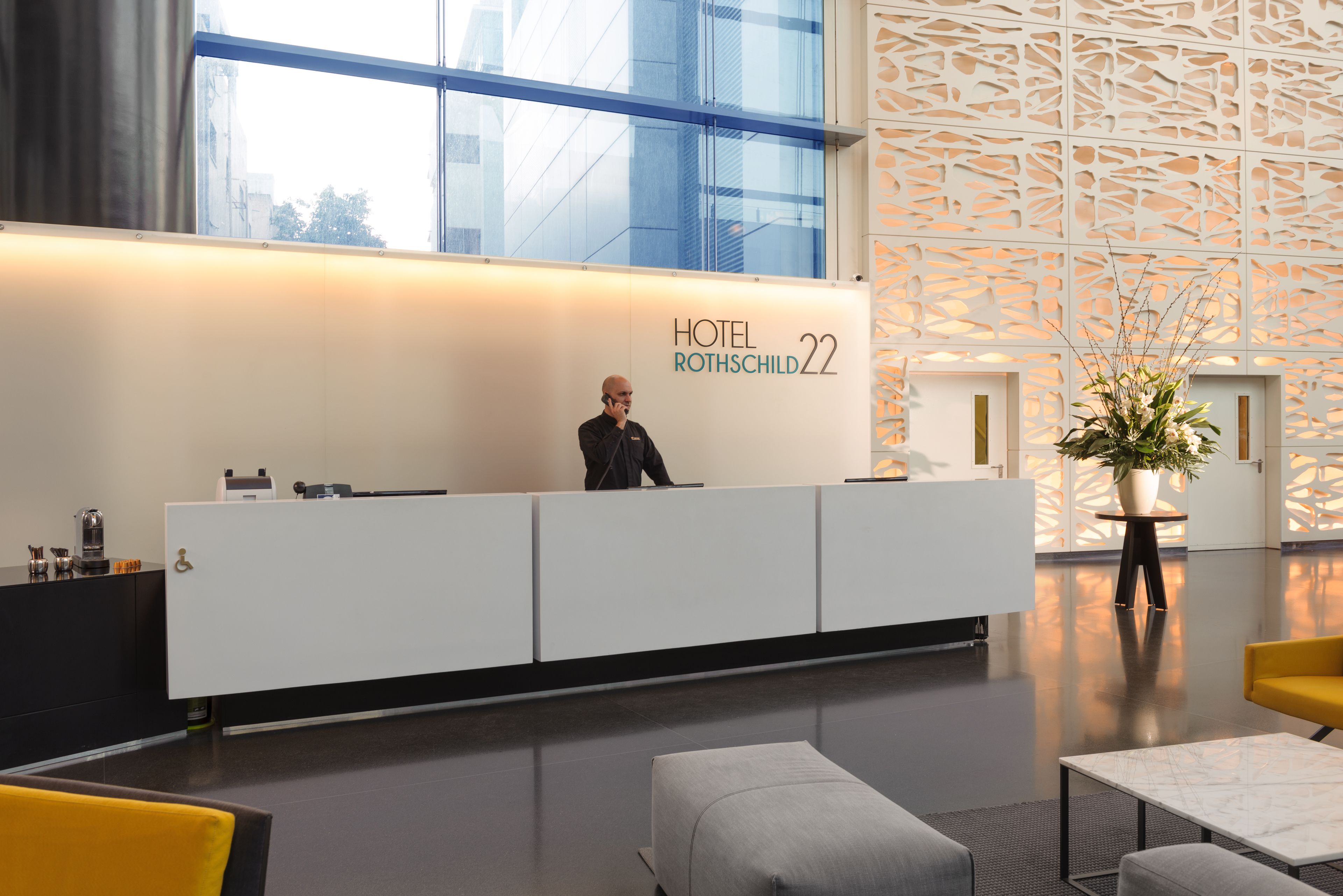 A hotel reception desk with a modern design, a receptionist, and a decorative plant.