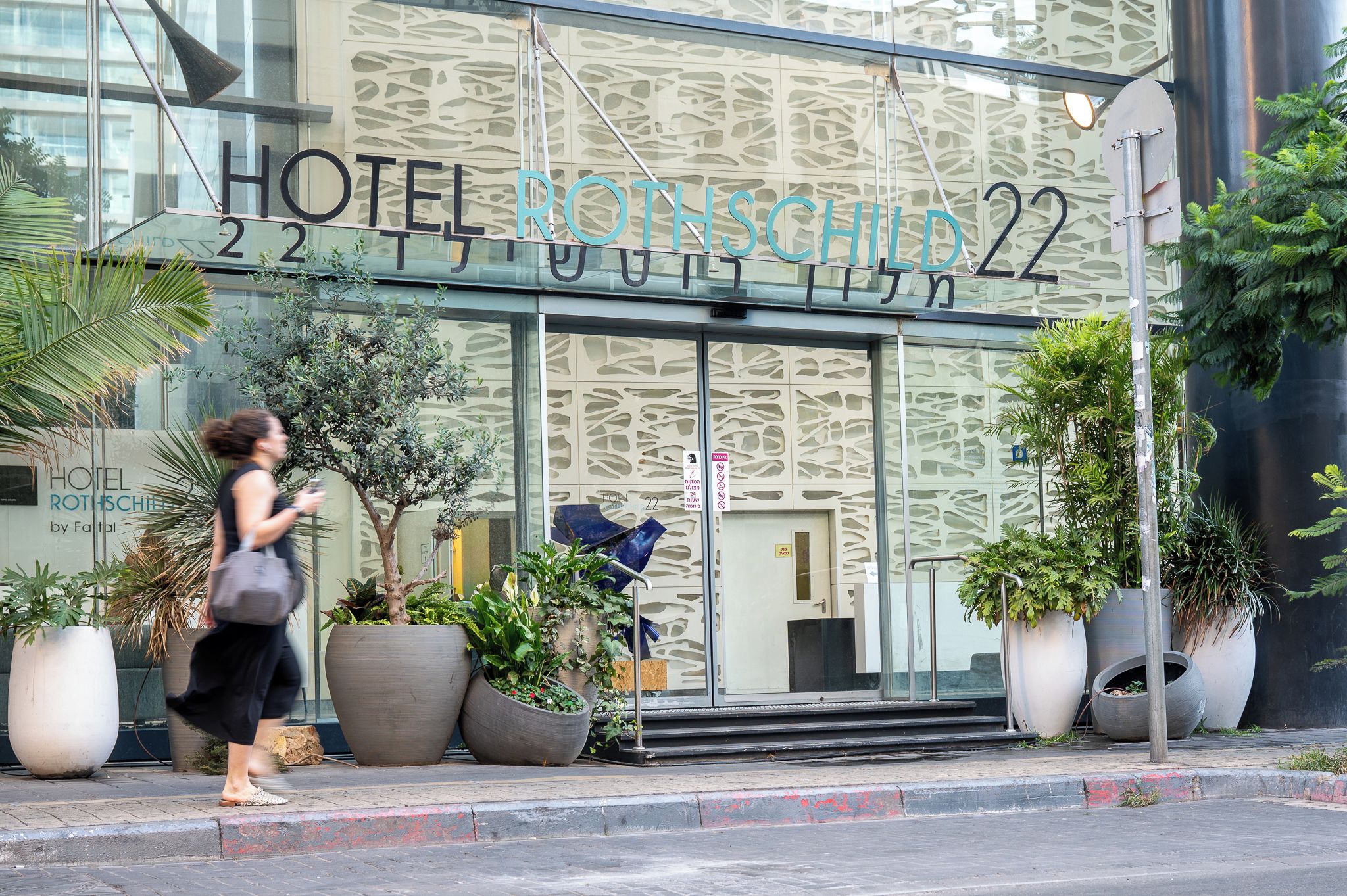 A hotel entrance with a modern facade, large potted plants, and a sign indicating the hotel name and room number.