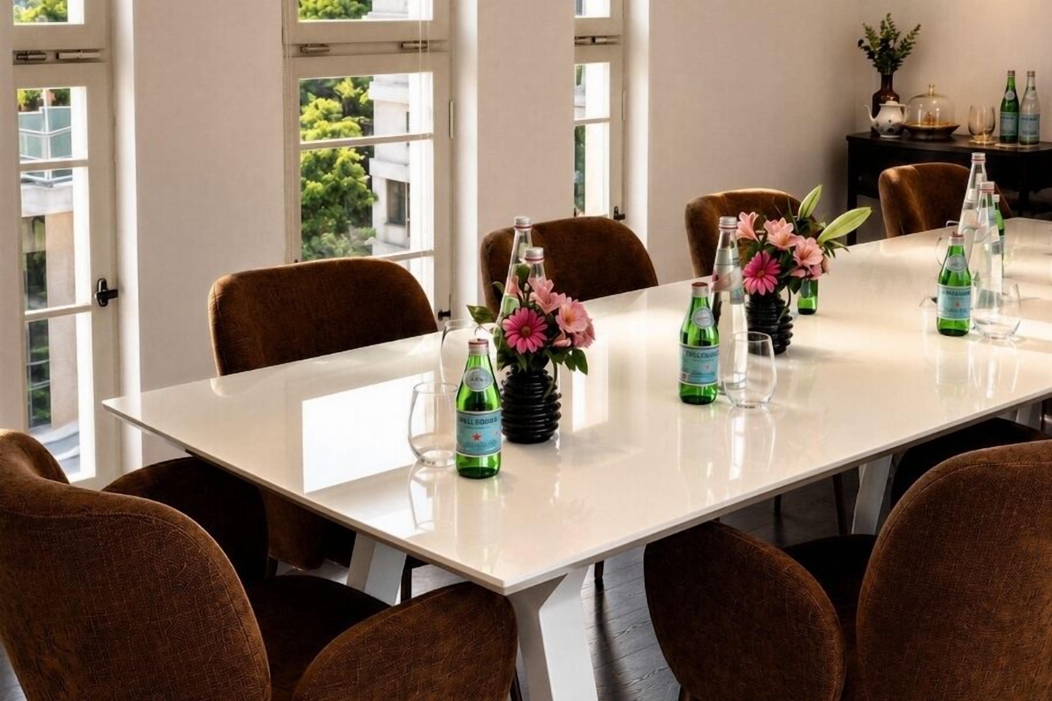Une table de conférence, des chaises, des bouteilles d’eau et un vase avec des fleurs.
