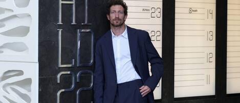 A man in a suit standing in front of a building with a large number '22' and the letters 'HI LD' visible.