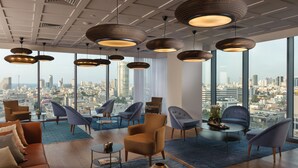A modern lounge with a city view, featuring a mix of sofas and armchairs, a coffee table, and pendant lighting. - Hotel Rothschild 22 - FATTAL COLORS (Tel Aviv)