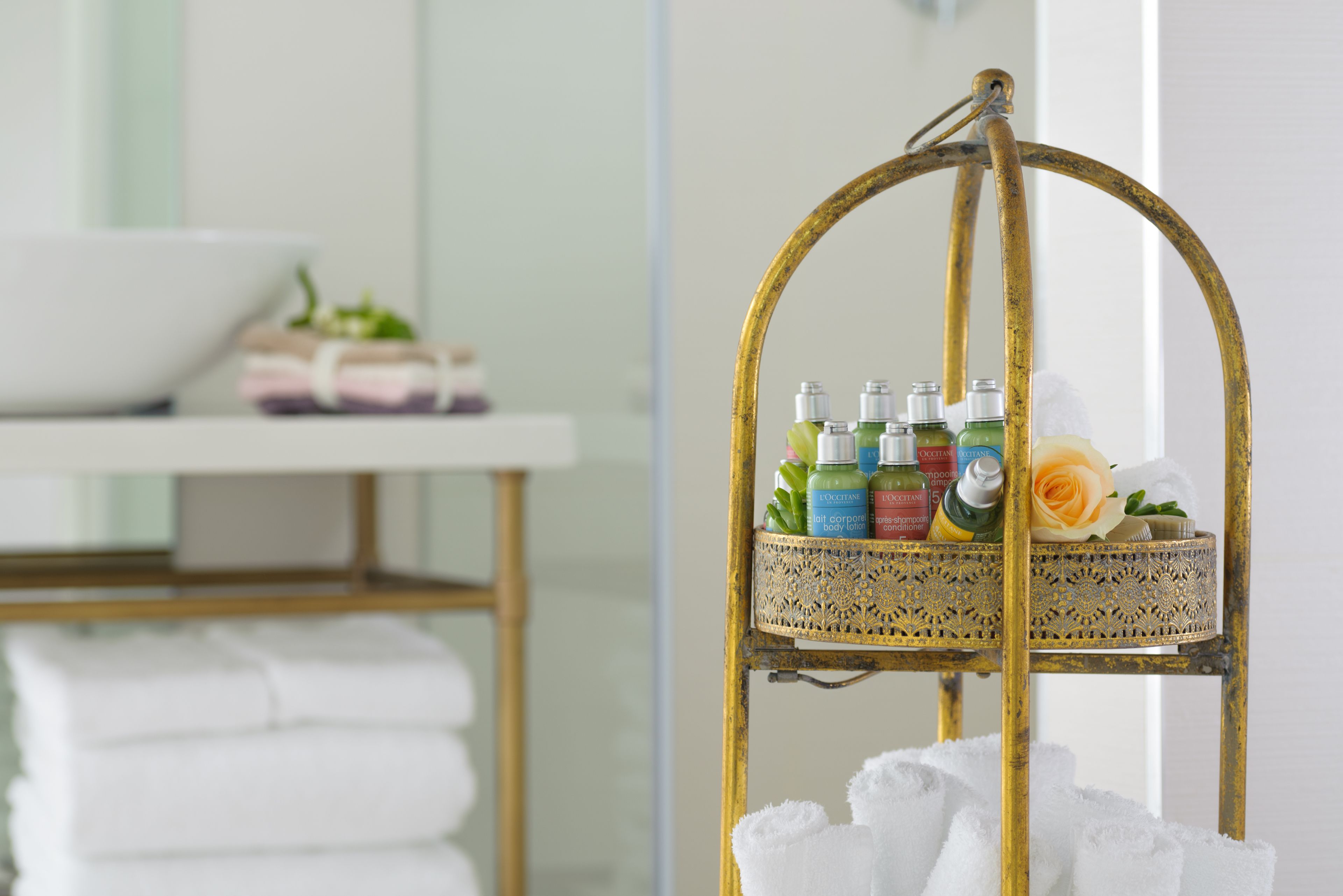 Un baño con una repisa dorada que sostiene artículos de tocador y una rosa.