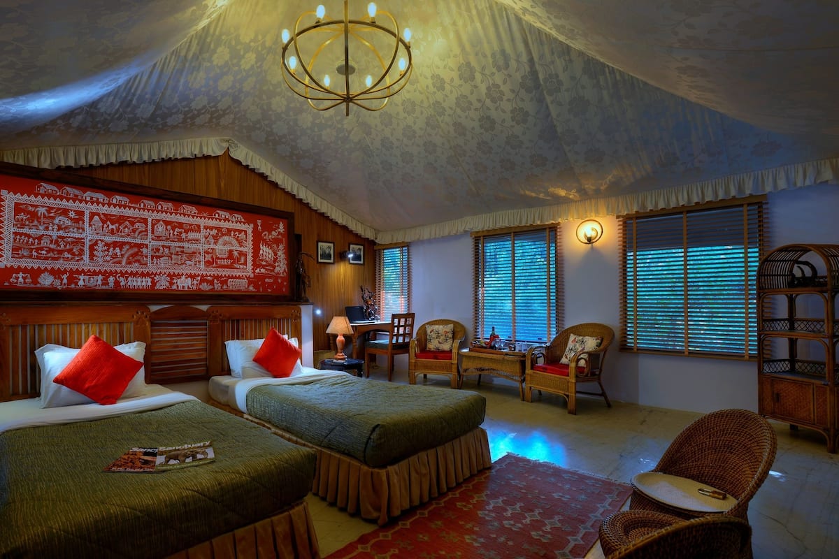 A room with two beds, a chandelier, a large tapestry, and a wooden bookshelf.