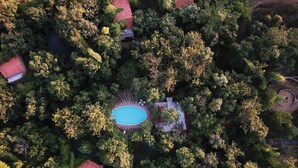 Vue aérienne d’un complexe hôtelier doté d’une piscine centrale, entouré d’une végétation luxuriante et de plusieurs bâtiments aux toits rouges.