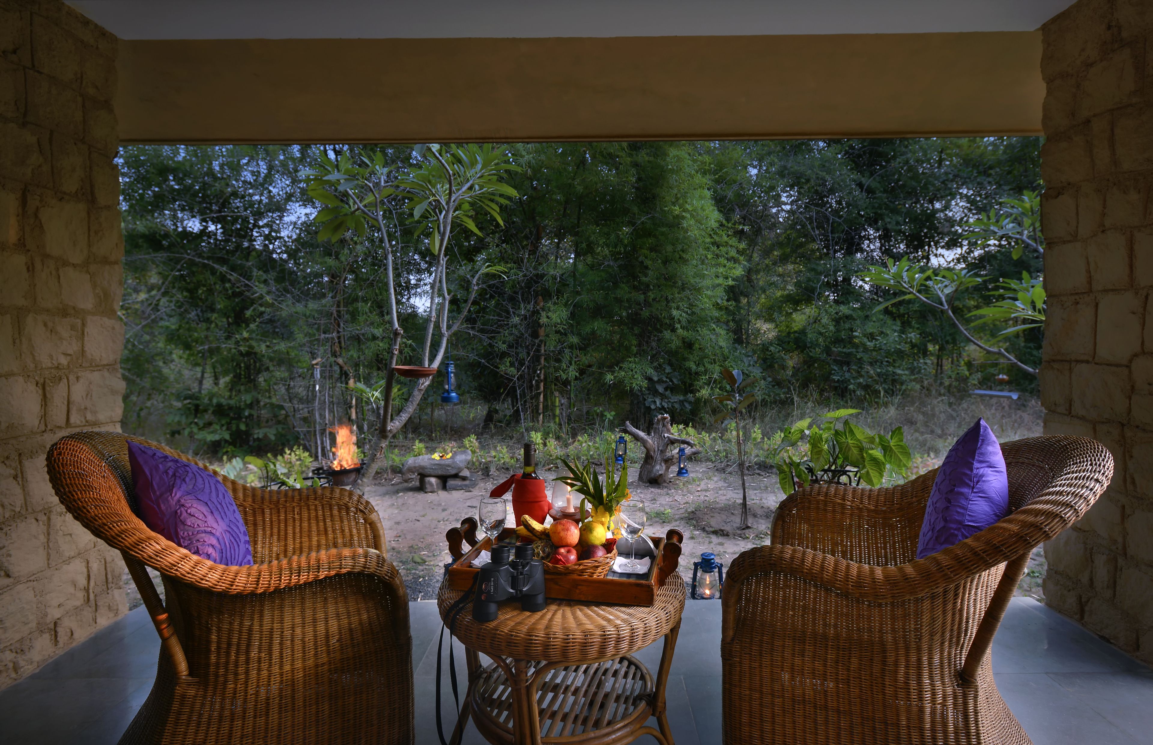 Un ensemble de meubles de jardin en osier, comprenant une chaise et une table, installé de manière à offrir une vue sur un jardin et un foyer extérieur.