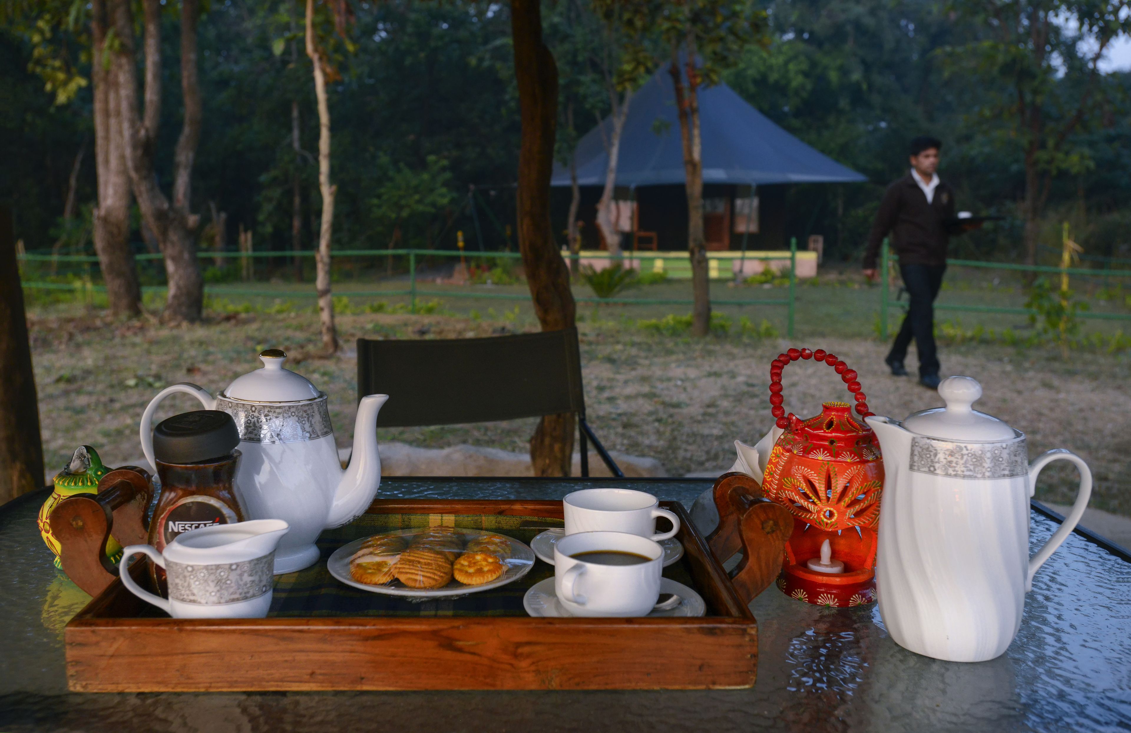 A tray with a teapot, cups, and pastries on a table outdoors.