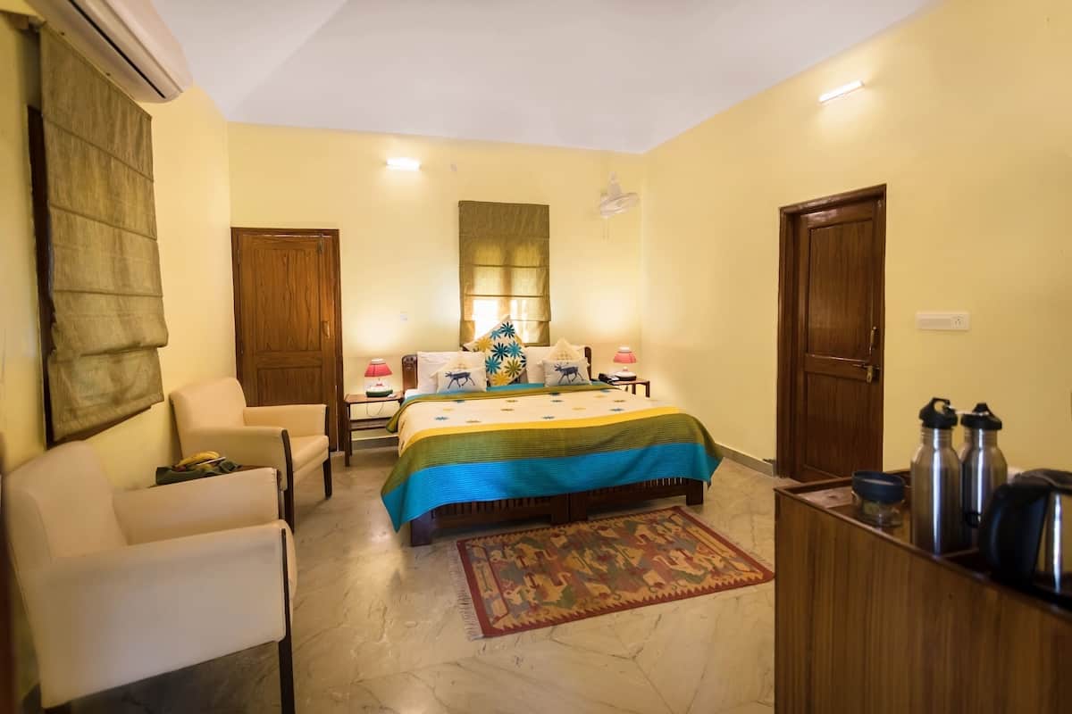 A bedroom with a bed, two chairs, a desk, an air conditioner, and a wooden door.