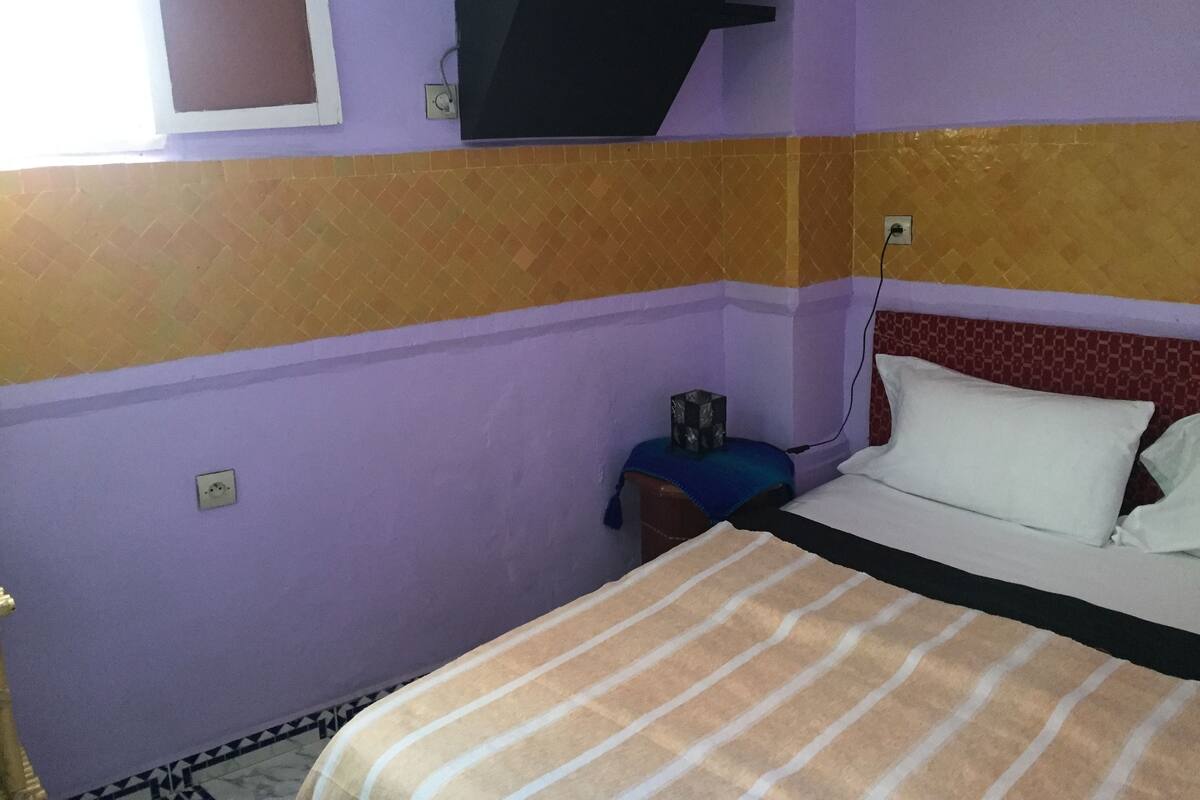 A room with a bed, a nightstand, a wall-mounted TV, and a window.
