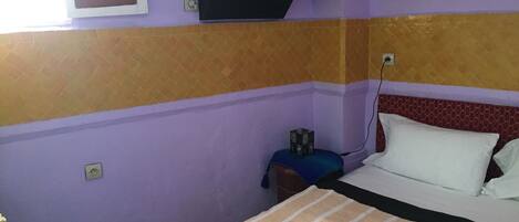 A room with a bed, a nightstand, a wall-mounted TV, and a window.