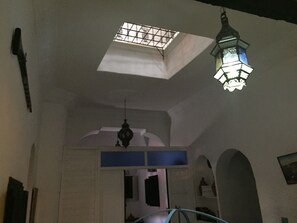 Una habitación con tragaluz, un farol colgante y un acceso a otra estancia.