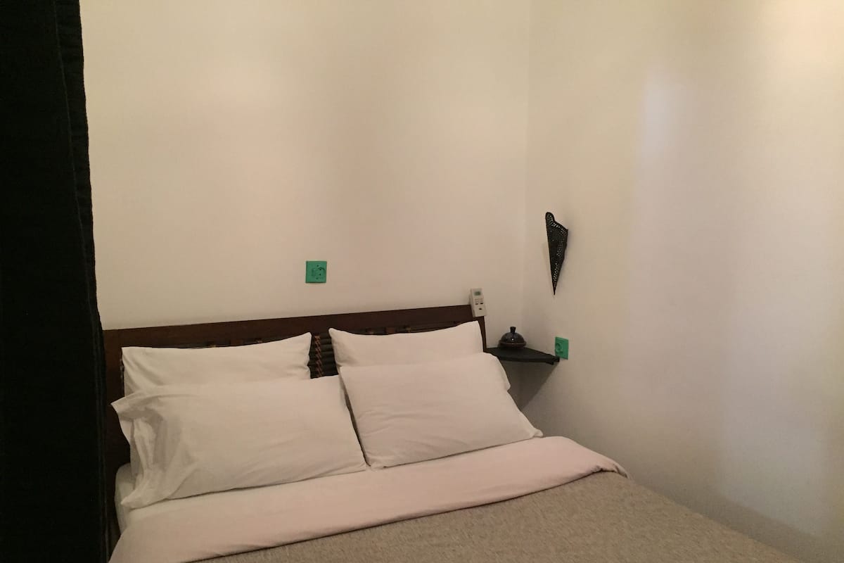 A standard hotel room with a bed, a nightstand, and a wall-mounted light fixture.