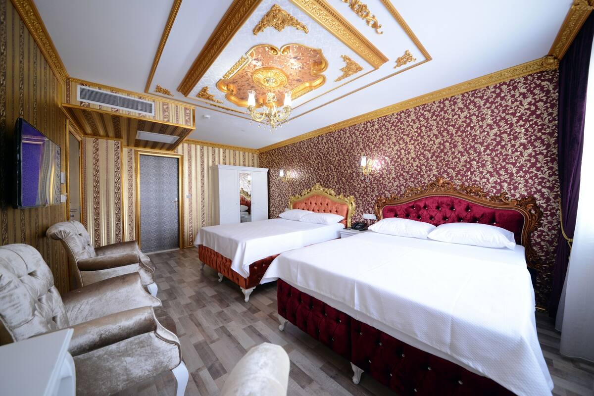 Habitación de hotel con dos camas, un área de descanso con sillas y un techo decorativo.