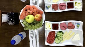 A table with a fruit and cheese platter, two bottles of water, and a napkin with cutlery. - Babel Park Hotel (Istanbul)