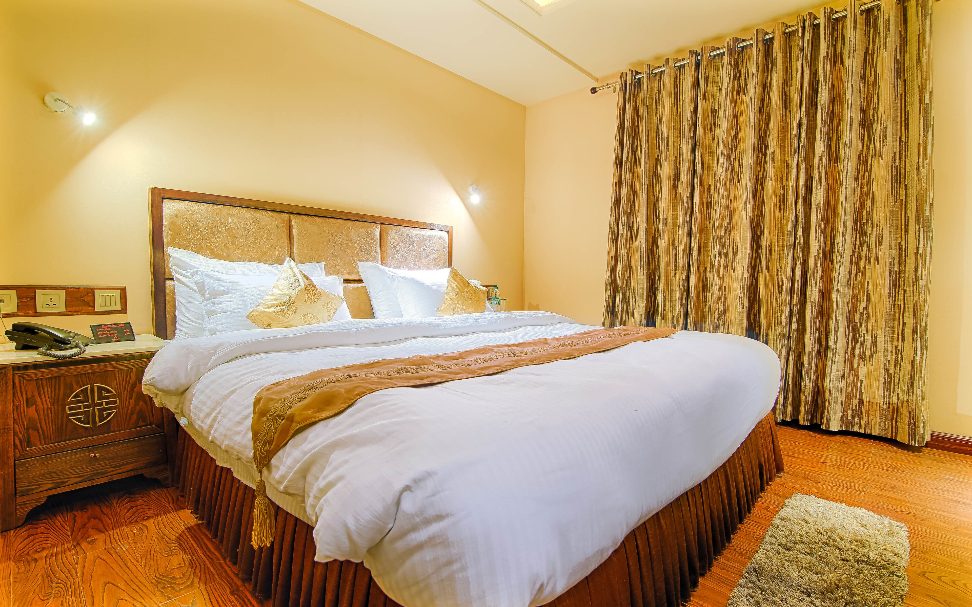 Una habitación de hotel con una cama grande, una mesita de noche de madera con un teléfono y una cortina con diseño vertical.