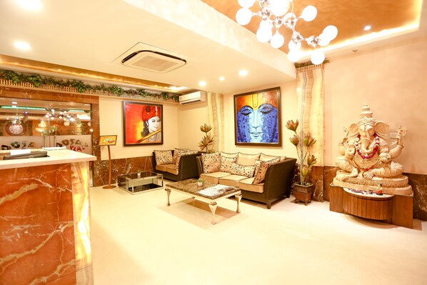 A well-lit hotel lobby with a marble reception desk, a sofa set, a coffee table, and a statue of a deity.