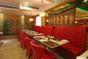 A restaurant with red booths, tables set with plates and cutlery, and a Buddha mural on the wall. - Divinity By Audra Hotels (Mathura)