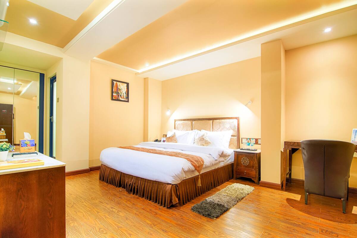 A hotel room with a large bed, a desk, a chair, and a small table.